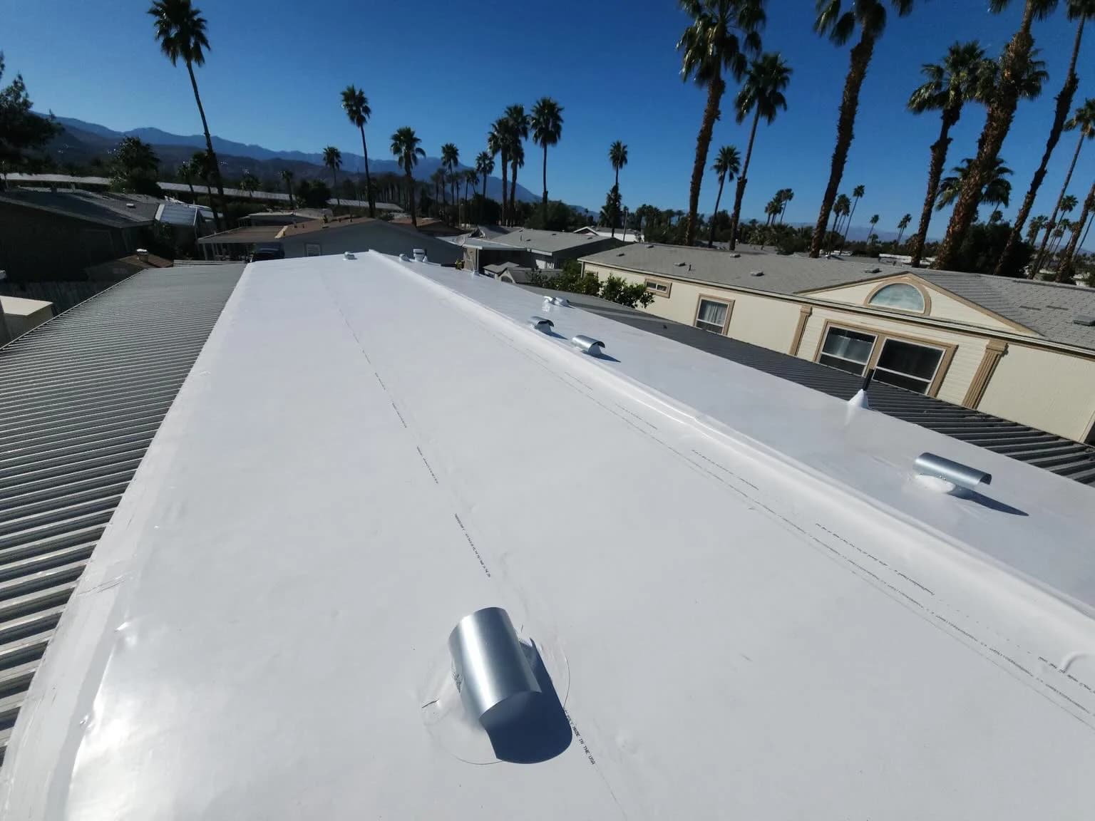 White low-slope roof with a raised center ridge and flashed pipe penetration